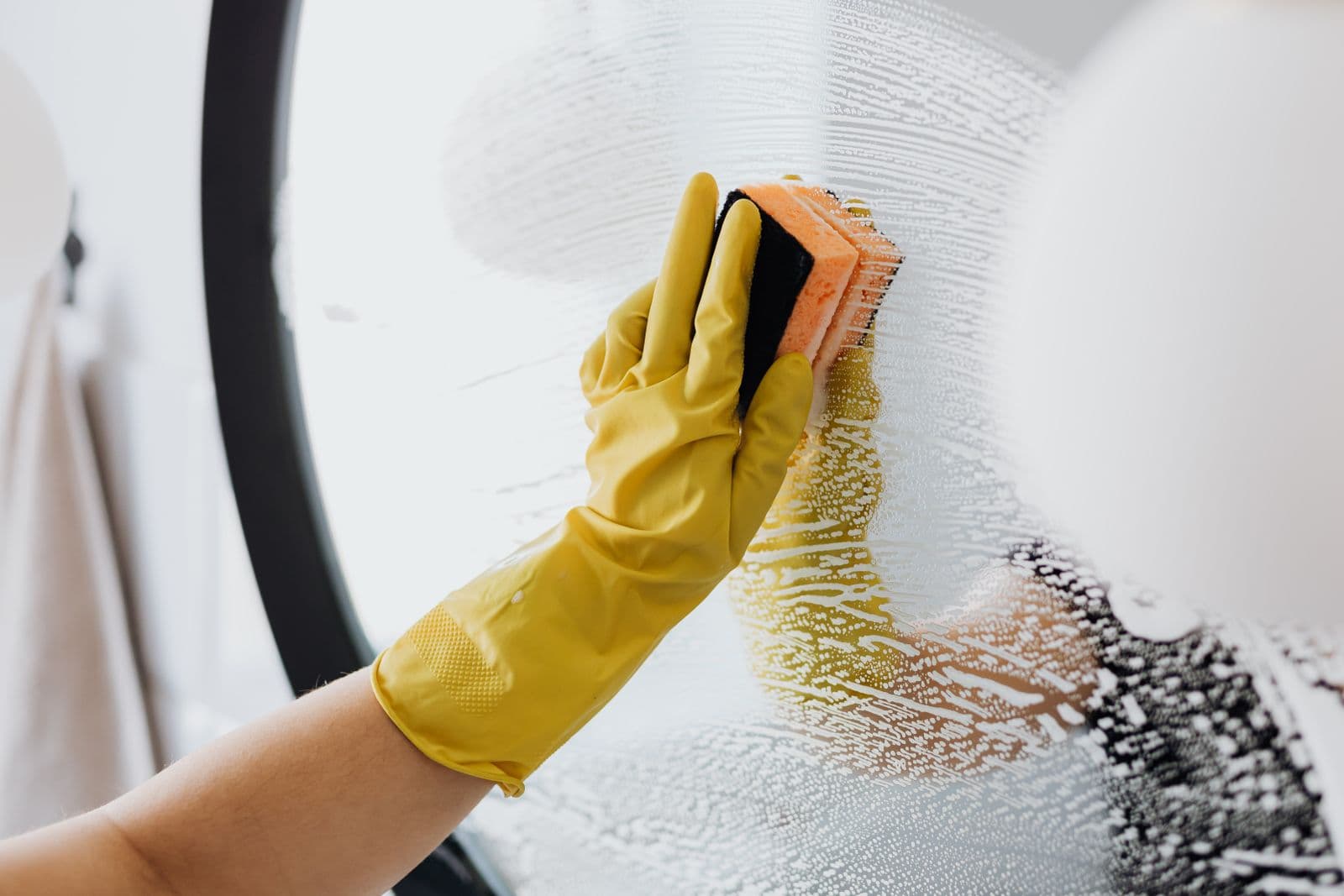 Nettoyage d'un miroir rond à l'éponge, gants jaunes et mousse